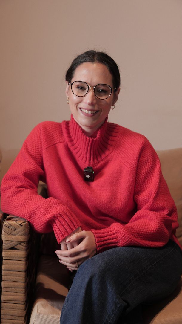 Gisell Acosta sonriendo en su consultorio, con anteojos y suéter rojo